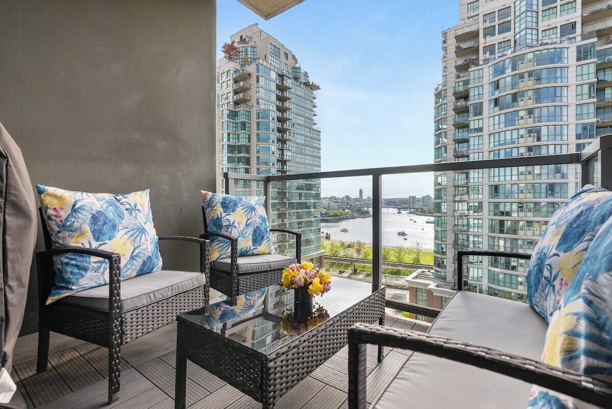 A balcony with wicker furniture, a glass table, and a view of high-rise buildings.