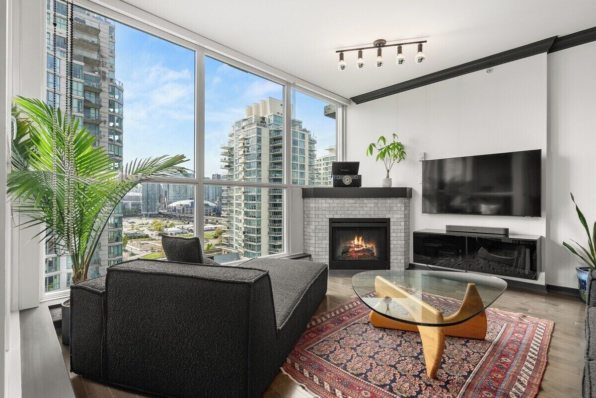 A modern living room with a fireplace, a large TV, and a view of high-rise buildings.