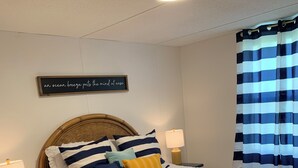 Ein ordentlich bezogenes Bett mit gestreifter Bettwäsche, ein Holz-Kopfteil, eine Nachttischlampe und ein dekoratives Schild an der Wand.