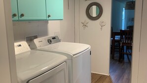 Ein Waschraum mit zwei weißen Waschmaschinen und Trocknern, turquoise farbenen Schränken, einem Spiegel und einer Meerstern-Dekoration an der Wand.