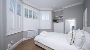 Ein Schlafzimmer mit einem Bett, weißen Fensterläden, einem Heizkörper, einem Spiegel und einem Regal mit Gegenständen.