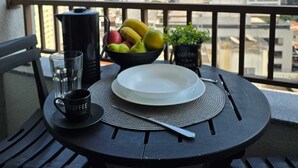 A balcony with a table set for breakfast, including a coffee mug, a bowl of fruit, and a plate. - Nik Paulista / comfort on a high floor and great location. (São Paulo)