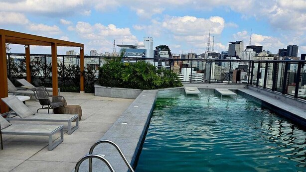 A rooftop pool with lounge chairs and a city skyline in the background. - Nik Paulista / comfort on a high floor and great location. (São Paulo)