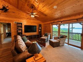 A log cabin interior with a large TV, wooden furniture, and a balcony with a view.