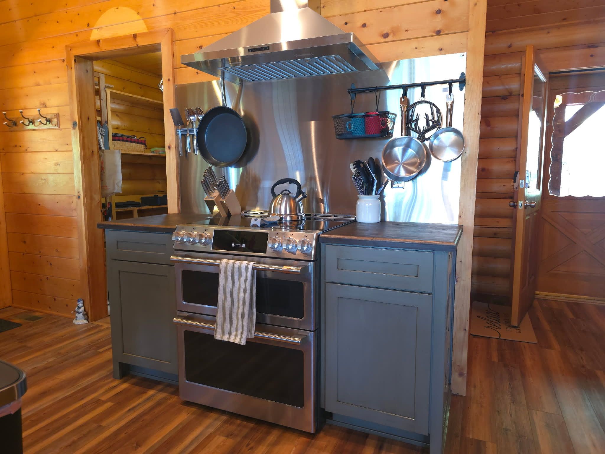 A compact kitchen with a stainless steel stove, oven, and a hanging pot rack.