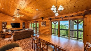 A log cabin interior with a dining area, a sofa, a TV, and a view of a lake.