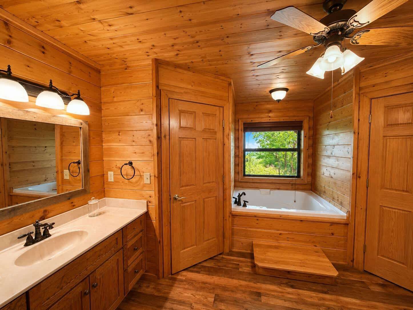A wooden cabin bathroom with a sink, mirror, vanity, bathtub, and a window.