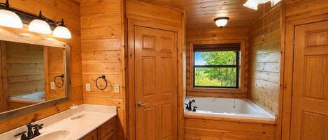 A wooden cabin bathroom with a sink, mirror, vanity, bathtub, and a window.