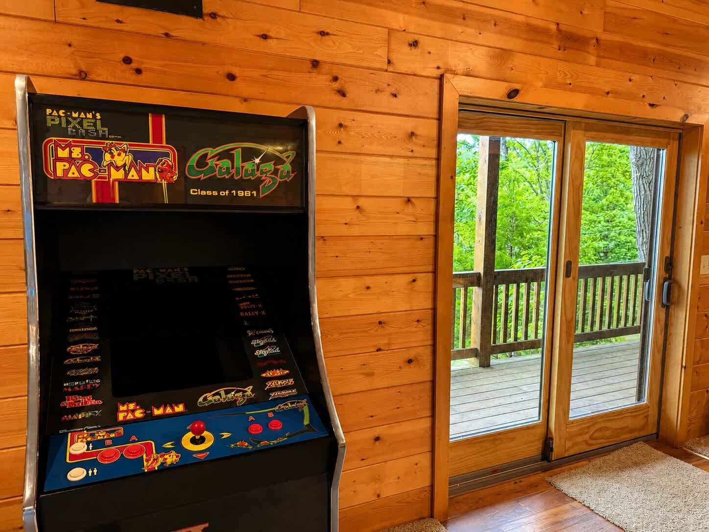 A Pac-Man arcade machine in a wooden cabin with a sliding glass door leading to an outdoor deck.