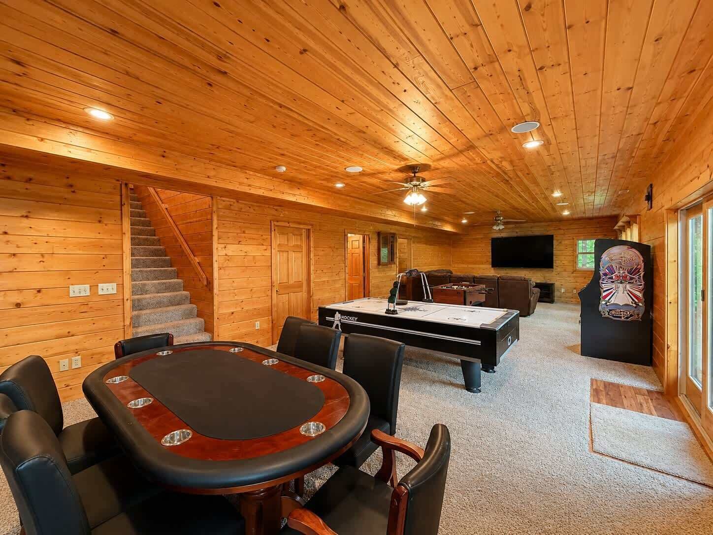 A wooden interior with a pool table, seating, and a staircase.