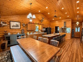 A wooden cabin interior with a dining area, kitchen, and a large window.