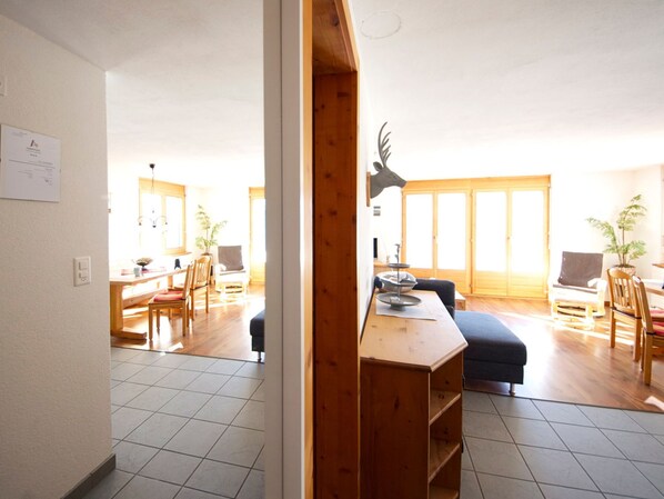 A spacious living area with a wooden dining table, chairs, a sofa, and a decorative deer head.