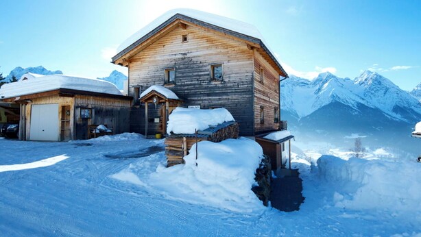 A wooden mountain lodge with a snow-covered roof, a garage, and a wooden staircase leading up to the entrance. - Chasa Aglia, (Ftan) by Interhome (Ftan)