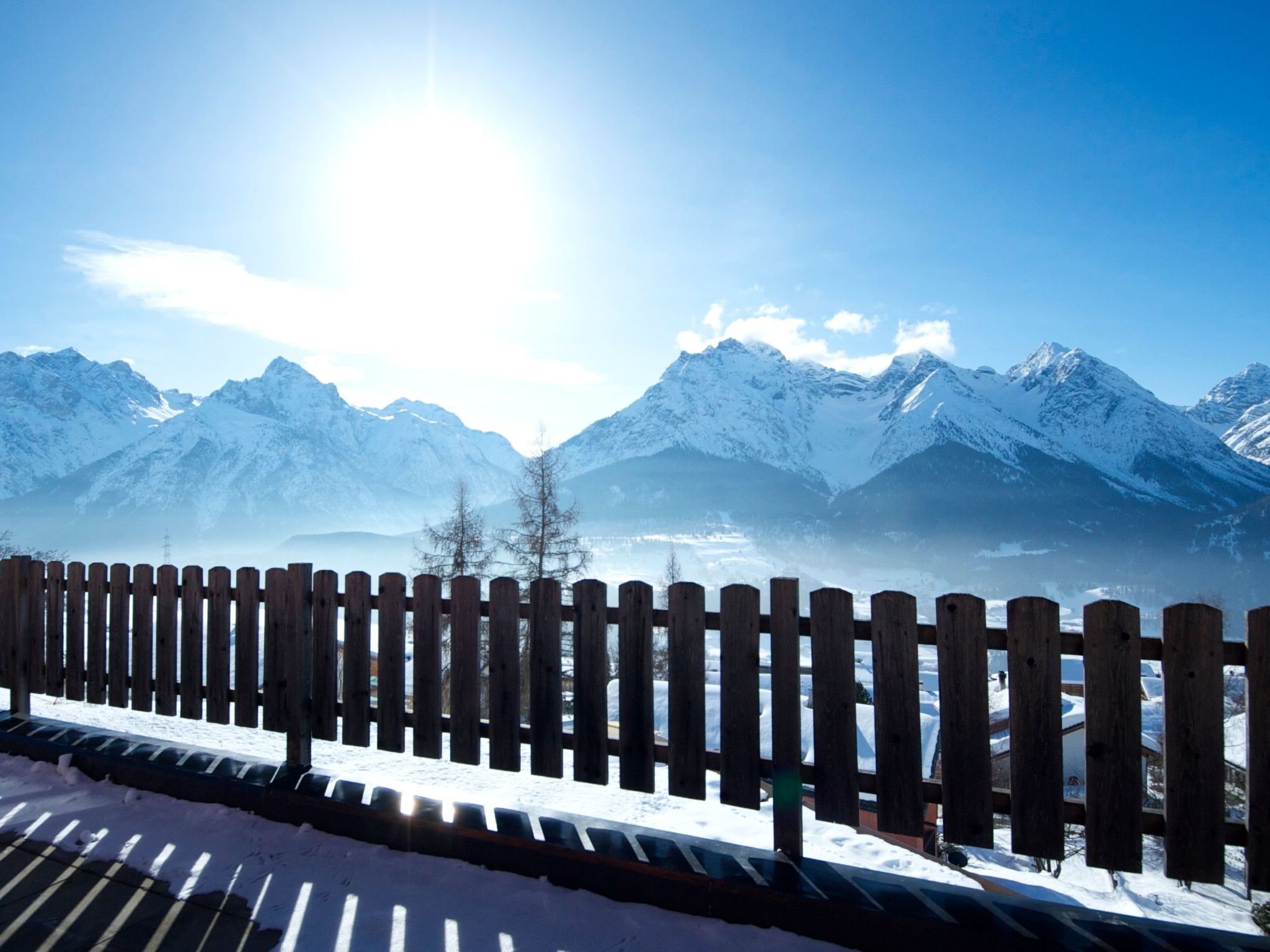 Een houten hek met een besneeerd landschap en bergen op de achtergrond.