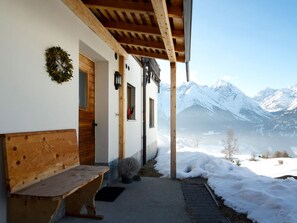 A wooden bench outside a building with a view of snow-covered mountains.