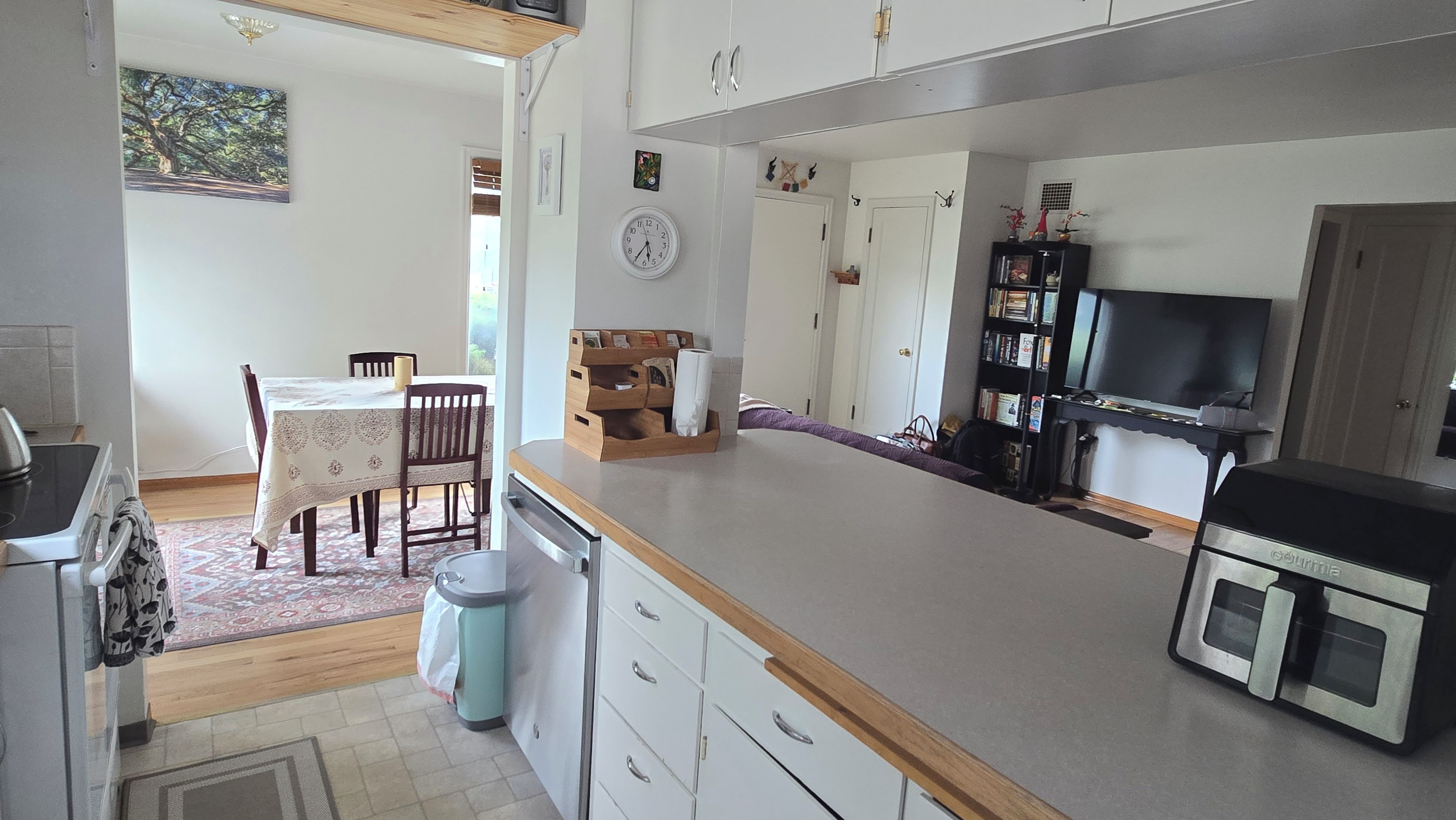Une cuisine avec une table à manger, des chaises, une horloge et un téléviseur.