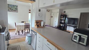 Une cuisine avec une table à manger, des chaises, une horloge et un téléviseur.