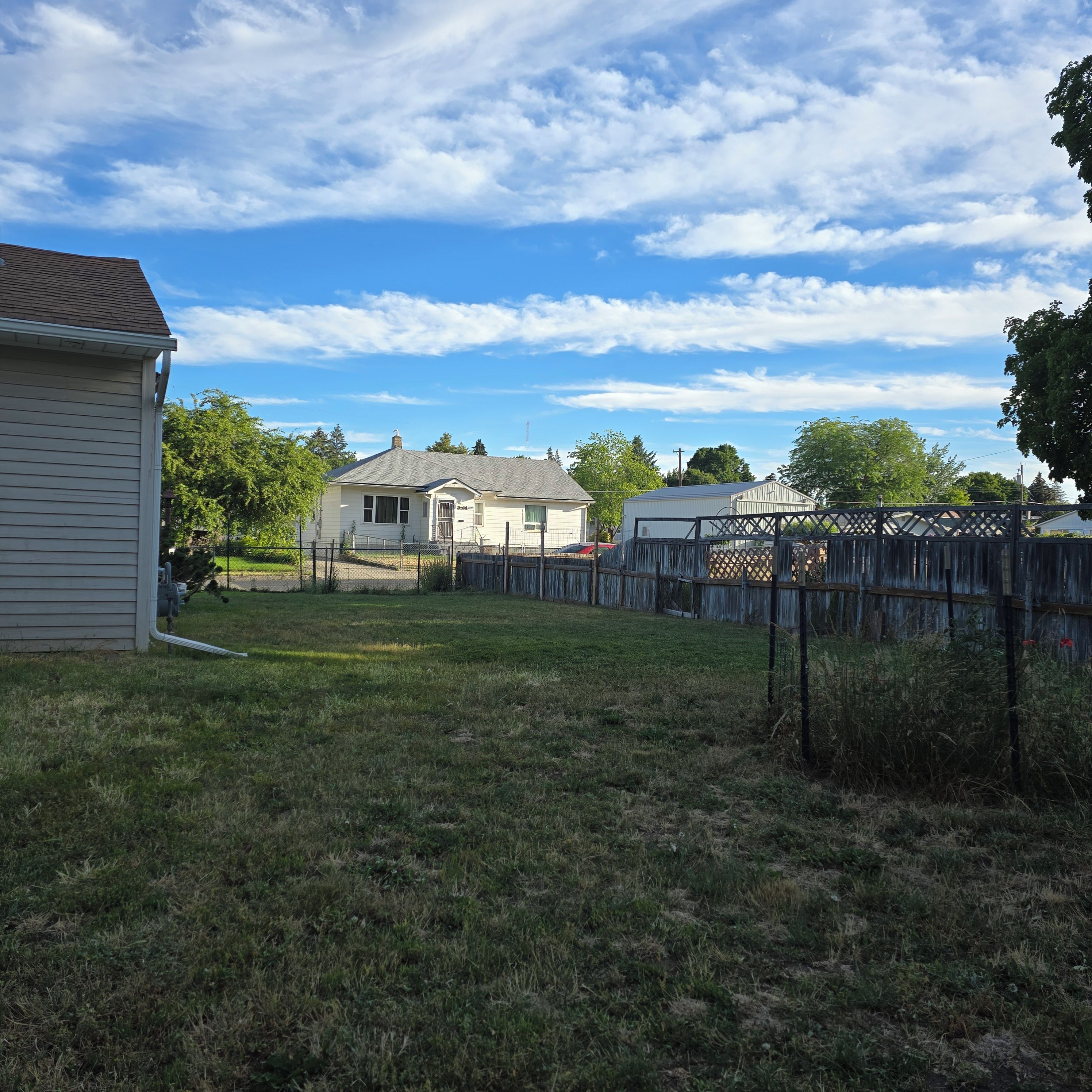 A residential area with a house, a fenced yard, and a clear sky.