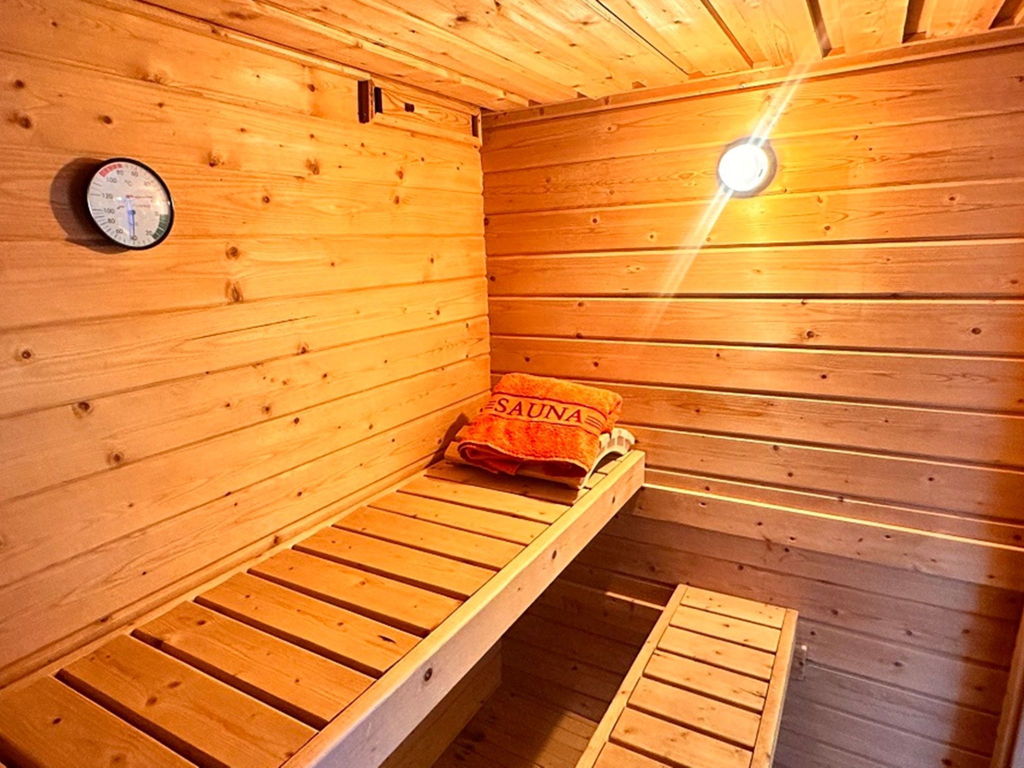 Een sauna met houten wanden, een bankje, een handdoek en een thermometer.
