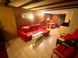 A room with a wooden floor, a red sofa, a white coffee table, and a dining area with a table and chairs.