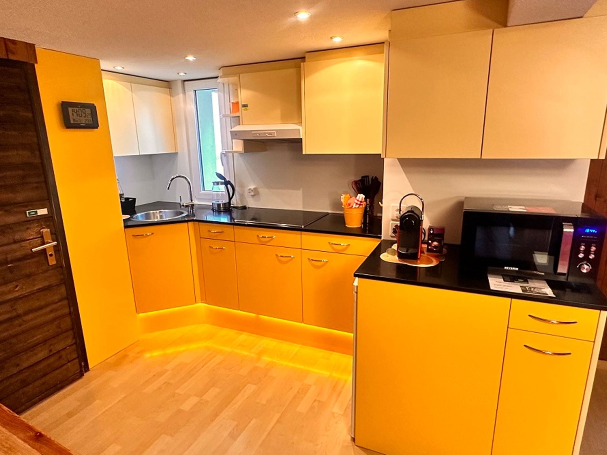 Une cuisine de taille réduite avec des meubles jaunes, un plan de travail noir et un four à micro-ondes.