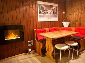 A wooden interior with a fireplace, a wooden table with red cushions, and a poster on the wall.