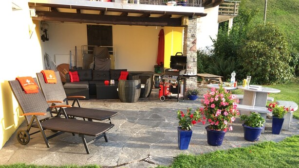 An outdoor patio with stone flooring, a barbecue grill, lounge chairs, and potted plants. - Bijouswiss - The Yellow House****, (Oberterzen), by Interhome (Oberterzen)