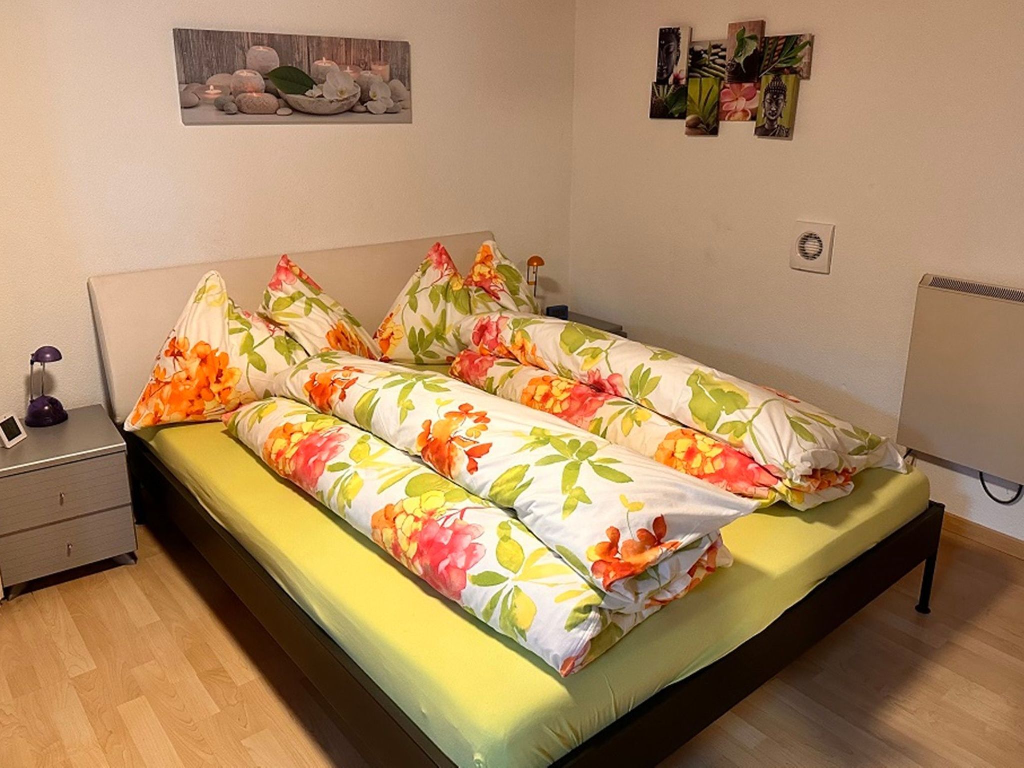 A bedroom with a bed, a nightstand, a wall-mounted artwork, and a radiator.