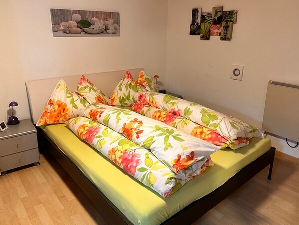 Een slaapkamer met een bed, een nachtkastje, een kunstwerk aan de muur en een radiator.