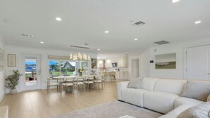 A modern living room with a large sofa, a dining area with a table and chairs, and a kitchen in the background. - Luxury Gulf-Access Retreat with Pool, Dock & Sunsets (Bonita Springs)