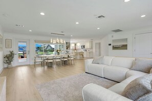 Ein modernes Wohnzimmer mit einer großen Couch, einem Essbereich mit Tisch und Stühlen sowie einer Küche im Hintergrund.