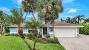 A residential property with a paved driveway, a garage, and a well-maintained lawn with palm trees. - Luxury Gulf-Access Retreat with Pool, Dock & Sunsets (Bonita Springs)