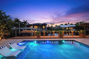 Ein Swimmingpool mit Liegestühlen, einer überdachten Terrasse und einem Sonnenuntergangshimmel.