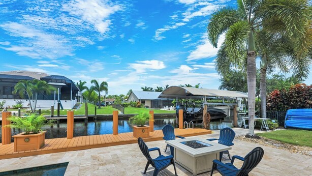 An outdoor patio with a pool, seating, and a view of a boat dock. - Luxury Gulf-Access Retreat with Pool, Dock & Sunsets (Bonita Springs)