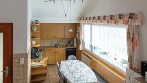 A compact kitchen with wooden cabinets, a dining table, and a window with curtains.