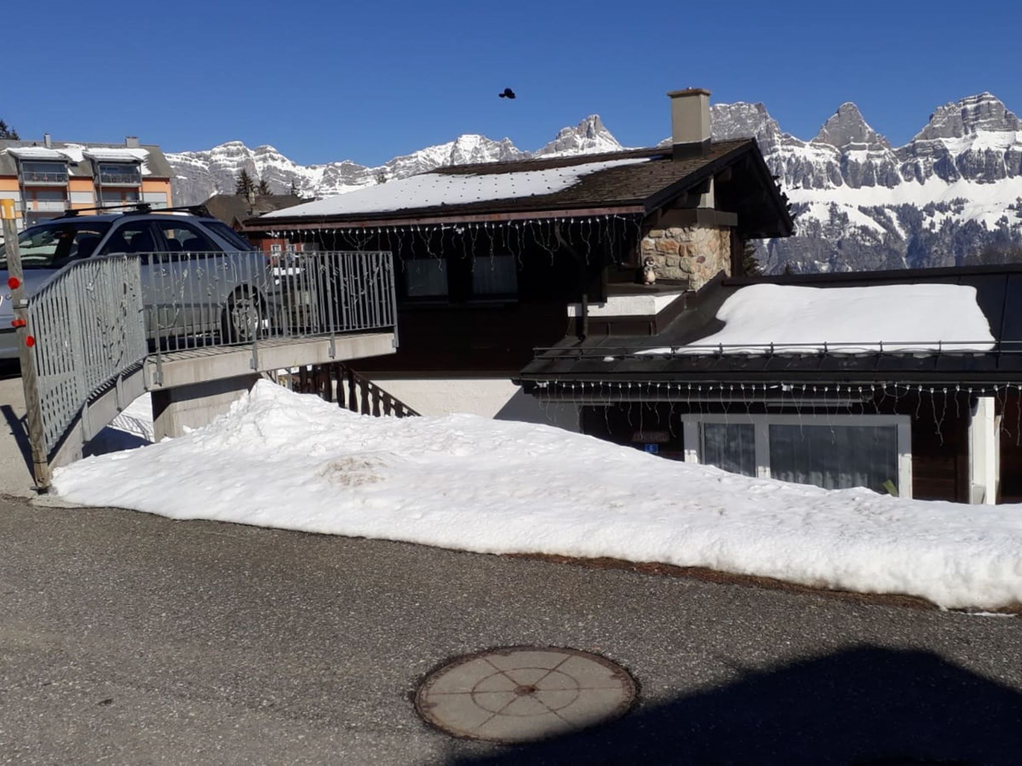 A snow-covered mountain landscape with a building featuring a wooden exterior and a metal staircase leading to a balcony.