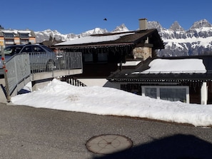 A snow-covered mountain landscape with a building featuring a wooden exterior and a metal staircase leading to a balcony.