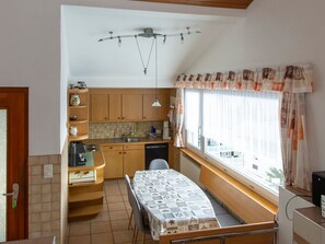 A compact kitchen with wooden cabinets, a dining table, and a window with curtains.