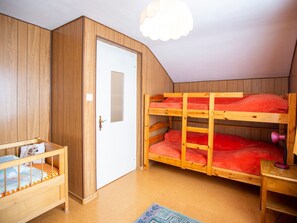 Una habitación con una cama litera, una cuna de madera pequeña y una puerta.