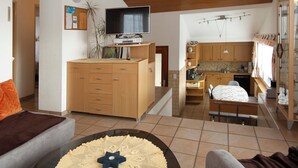 A modern living room with a sofa, a coffee table, a TV, and a kitchen in the background.