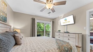 Ein Schlafzimmer mit Bett, Deckenventilator, Fernseher, Kommode und Blick ins Freie.