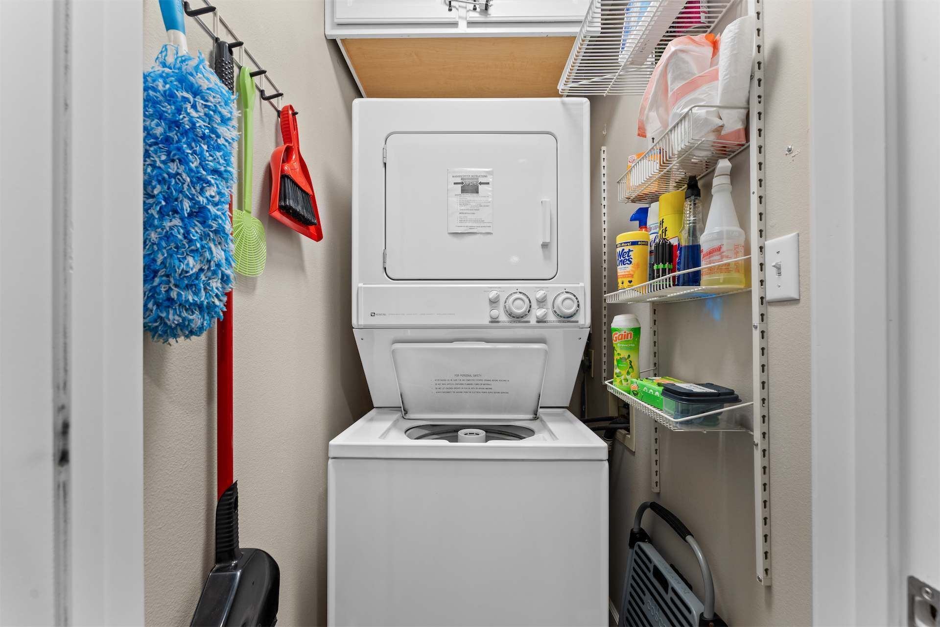 Une petite buanderie équipée d’un lave-linge et d’un sèche-linge superposés, d’un porte-serpillère et d’étagères contenant des produits de nettoyage.