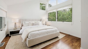 Una camera da letto con un letto grande, un comodino, una finestra vista alberi e una luce a soffitto.