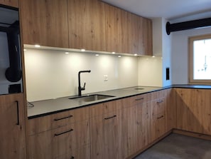 A modern kitchen with wooden cabinets, a black countertop, and a stainless steel sink. - La Rösa, (Sta. Maria Val Müstair) by Interhome (Sta. Maria GR)