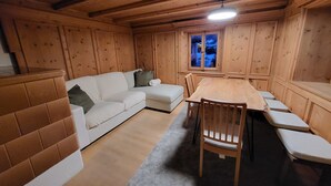 A cozy room with a wooden ceiling, a white sofa, a dining table with chairs, and a window with a view. - La Rösa, (Sta. Maria Val Müstair) by Interhome (Sta. Maria GR)