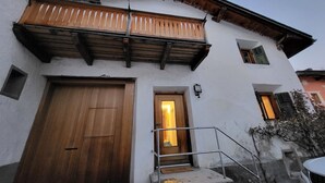 A two-story building with a wooden balcony, a large wooden door, and a small window with shutters. - La Rösa, (Sta. Maria Val Müstair) by Interhome (Sta. Maria GR)