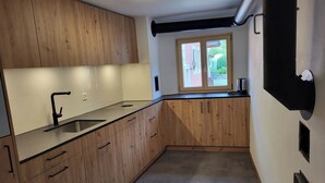 A kitchen with wooden cabinets, a black faucet, a window, and a black wall-mounted device. - La Rösa, (Sta. Maria Val Müstair) by Interhome (Sta. Maria GR)