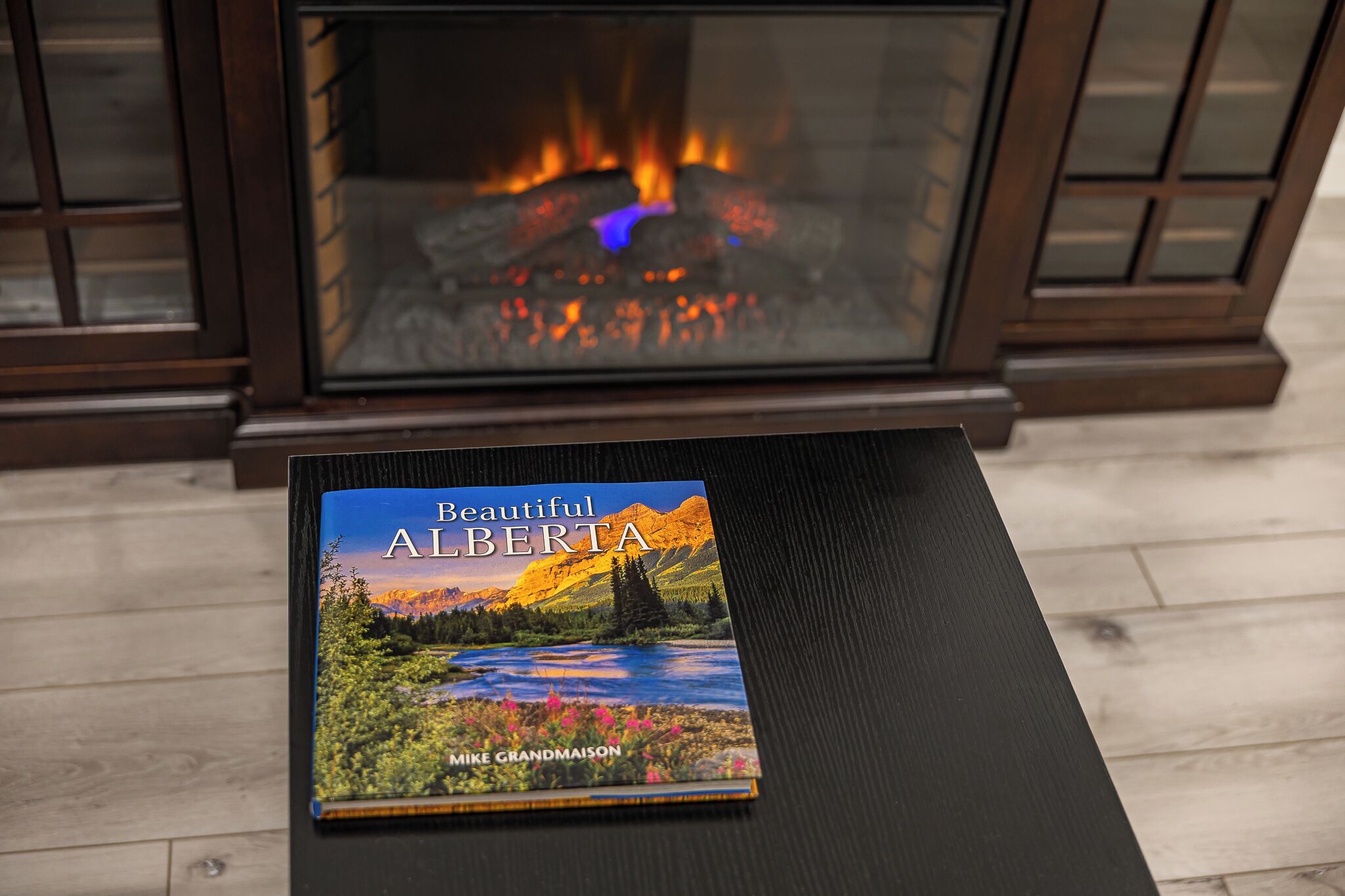 Un libro titulado 'Beautiful Alberta' sobre una mesa con una chimenea al fondo.