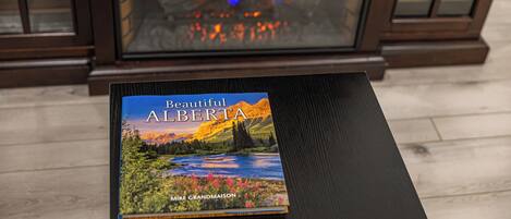 Un libro titulado 'Beautiful Alberta' sobre una mesa con una chimenea al fondo.