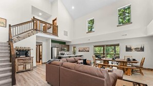 A spacious living area with a wooden staircase, a large sofa, a dining table, and a kitchen in the background. - Lakesides Retreat With Amenities (Hollister)